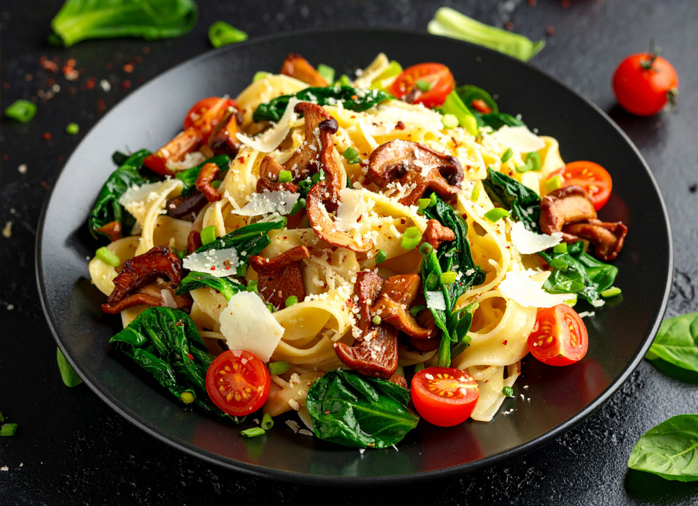 schwarzer Teller mit Penne mit Pilzen, Feldsalat und Tomaten - Bild KI-generiert